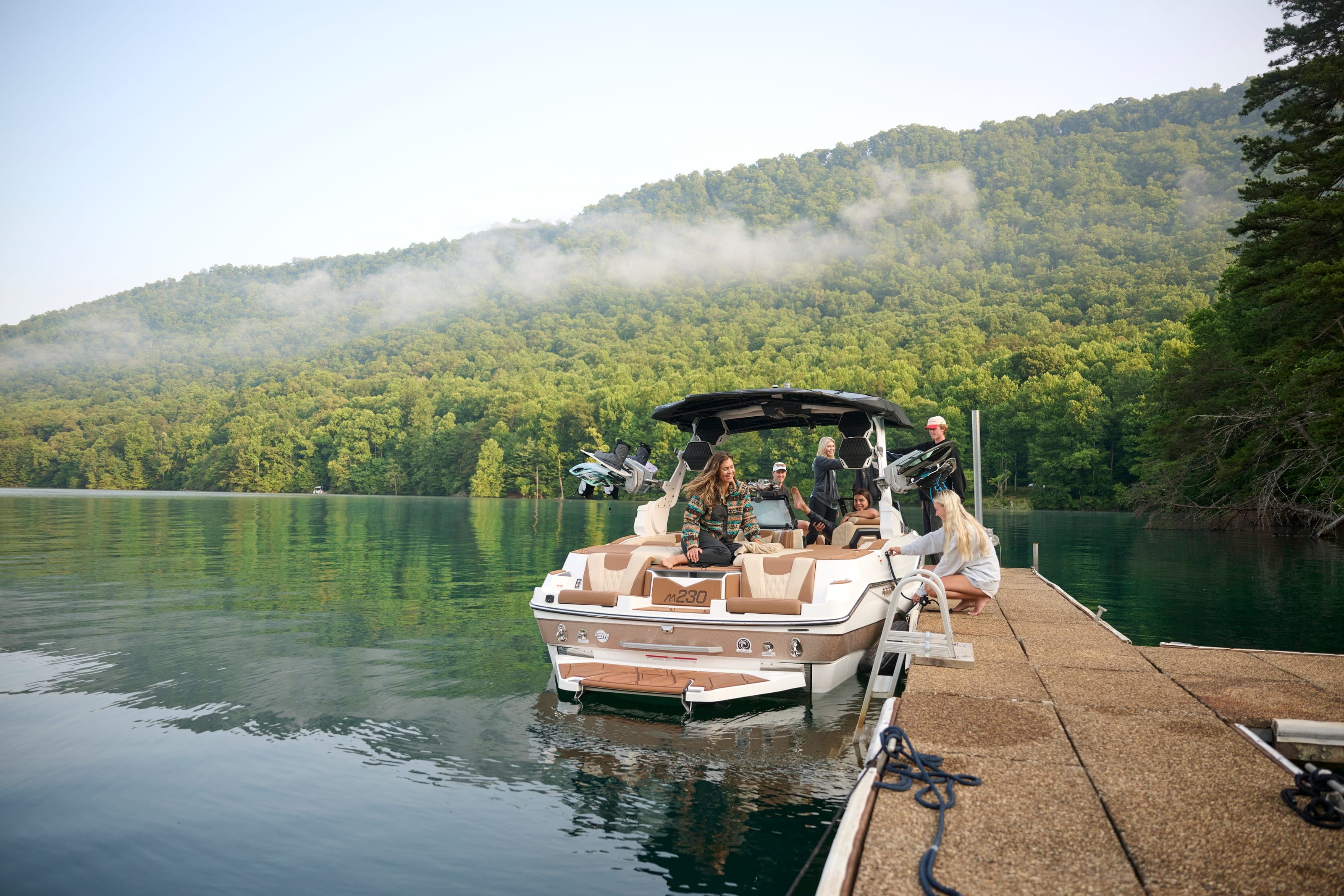 A Malibu M230 tied up at a dock on a still, misty morning