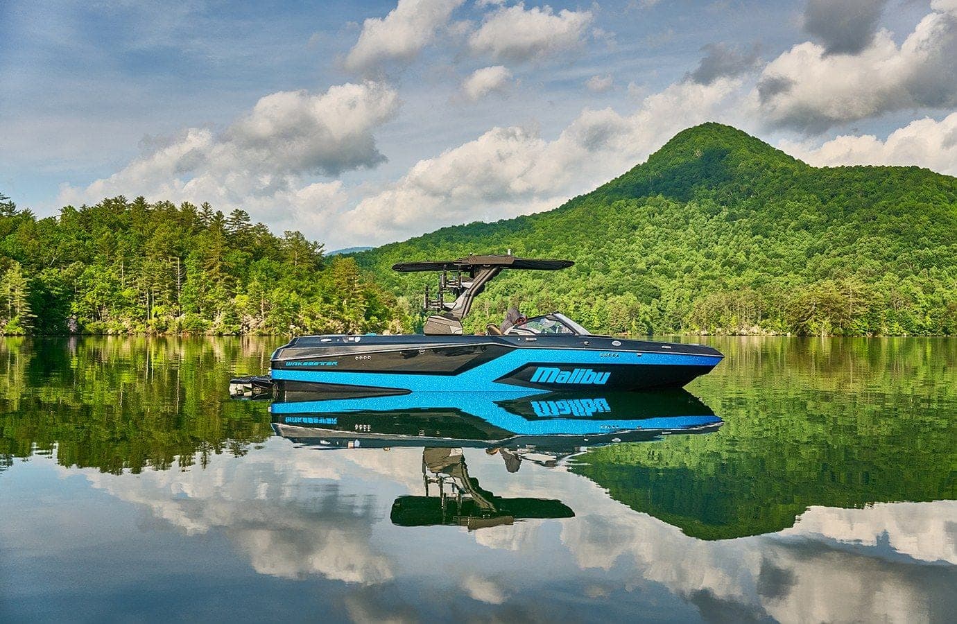 A Malibu 24 MXZ on calm water beneath a wooded mountain
