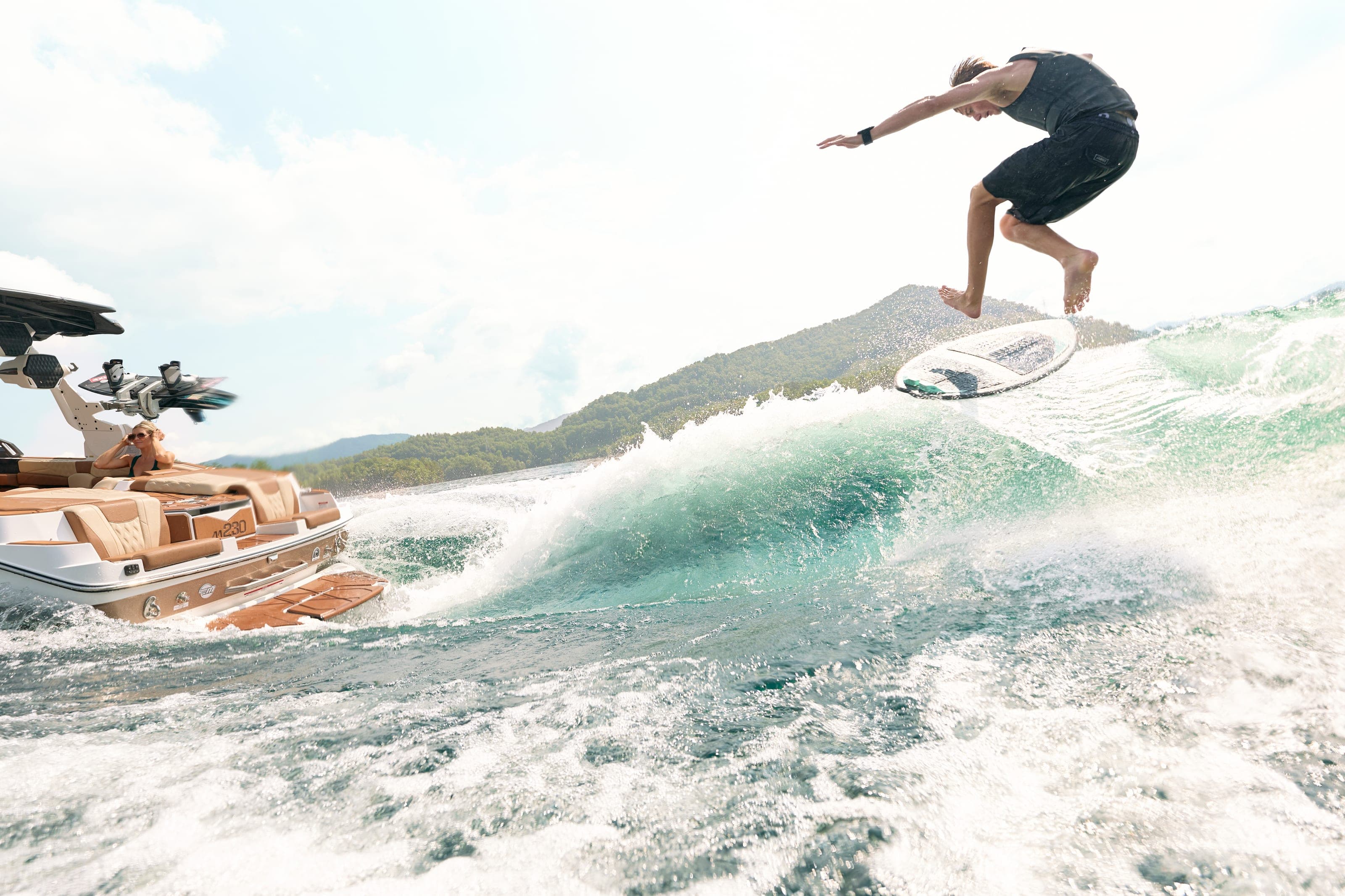 A rider in the air above the wave behind a Malibu M230