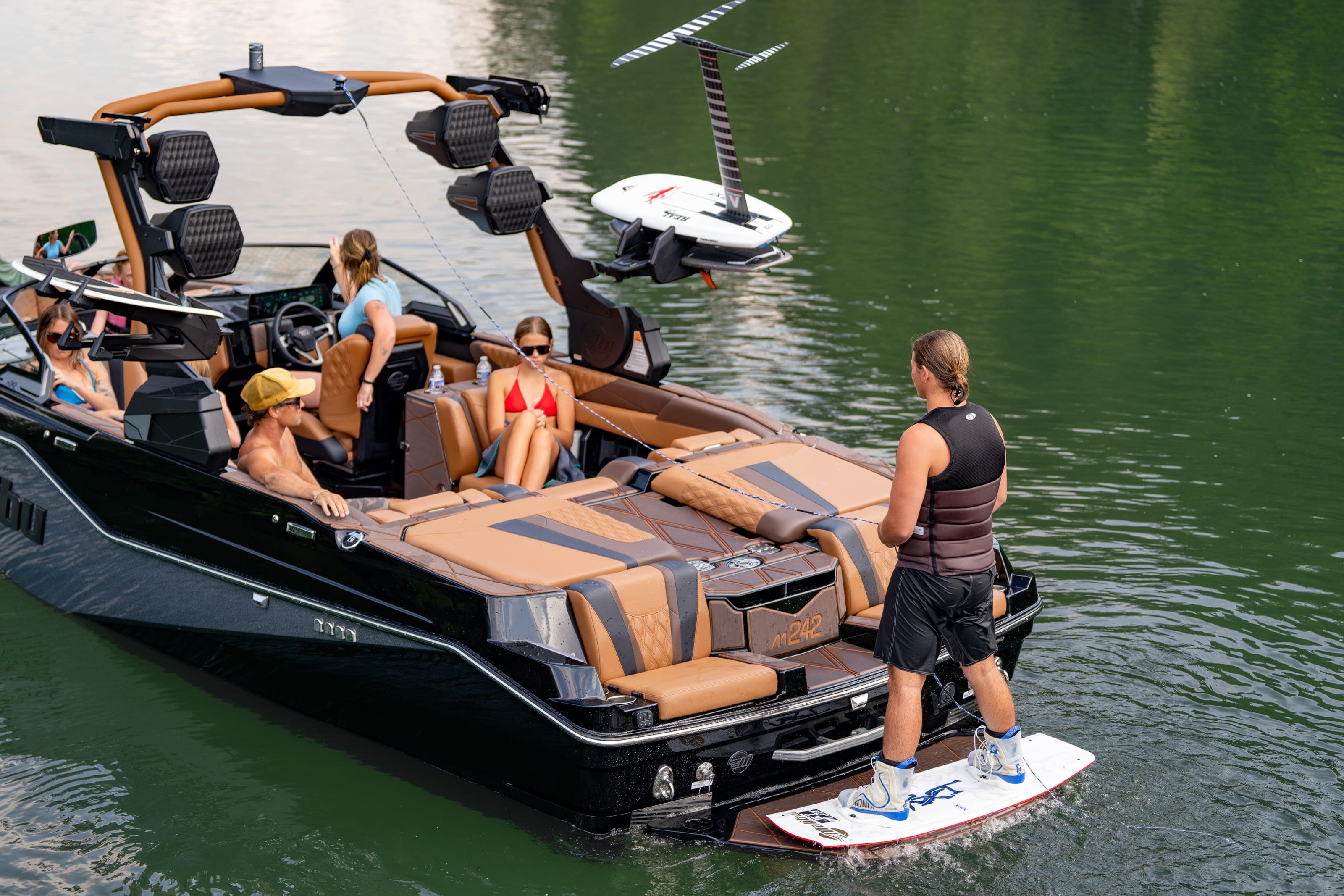 A woman stands on the swim platform of a Malibu M242 beside a board, friends in the rear seats