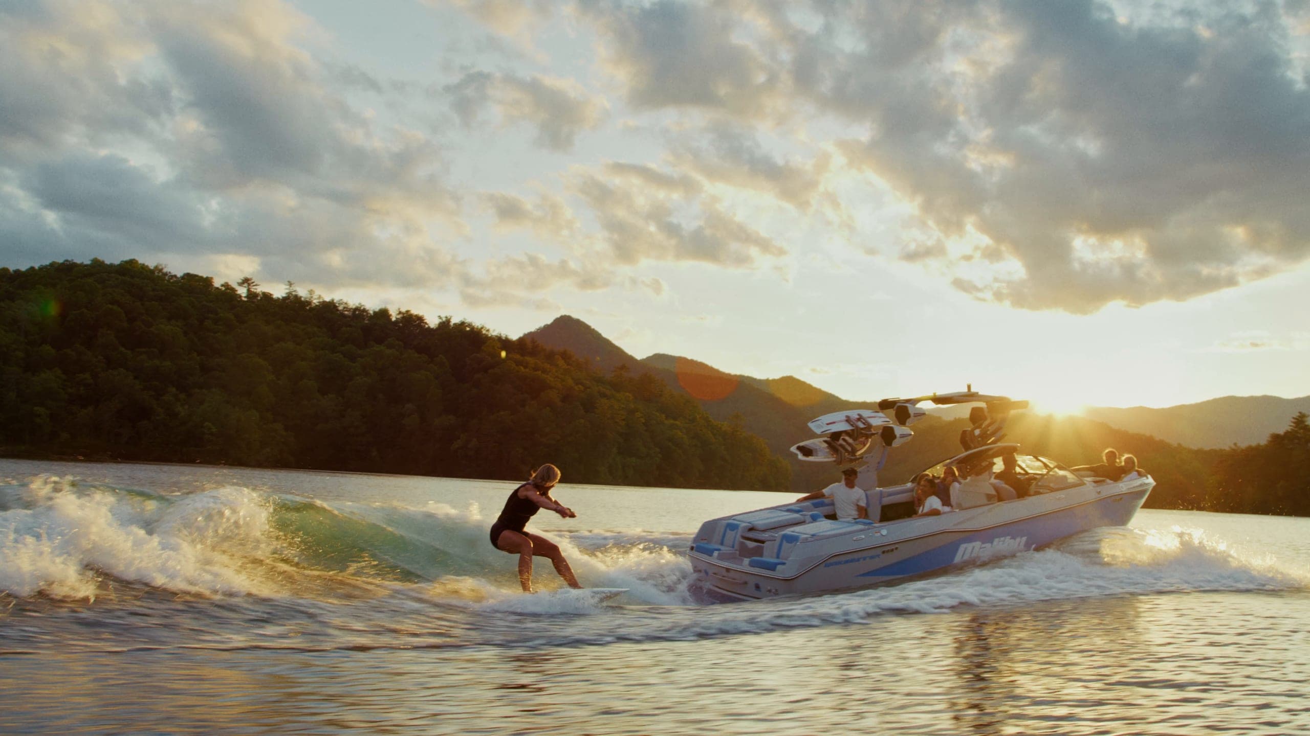 A Malibu 25 LSV carves a turn, a rider surfs its wave at sunset, and friends jump from the boat