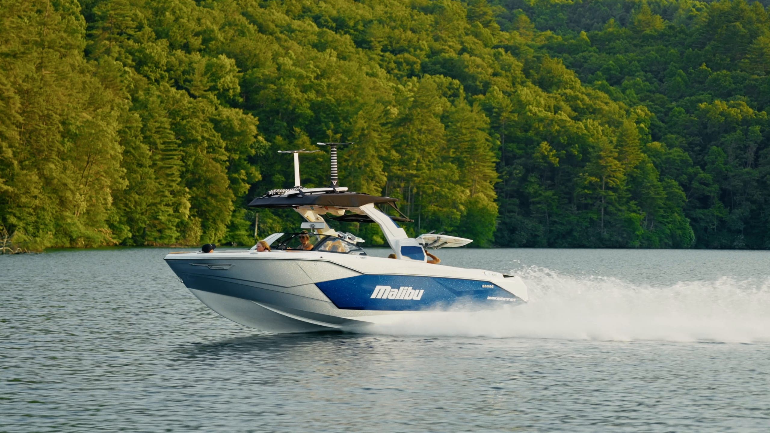 A rider surfing behind a Malibu 26 LSV, the boat from above with people aboard, and the boat at speed