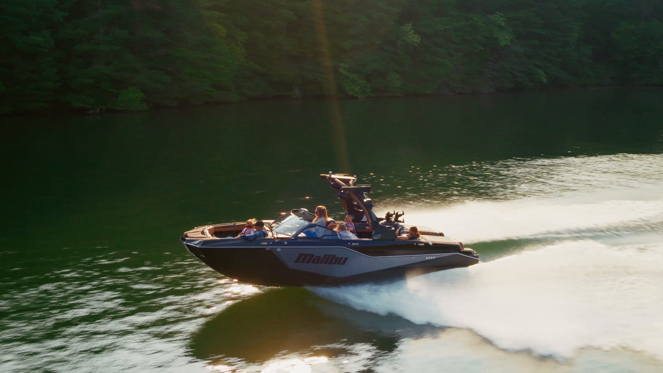 The helm of a Malibu M242, a rider surfing its wave, then the boat at speed in low sun