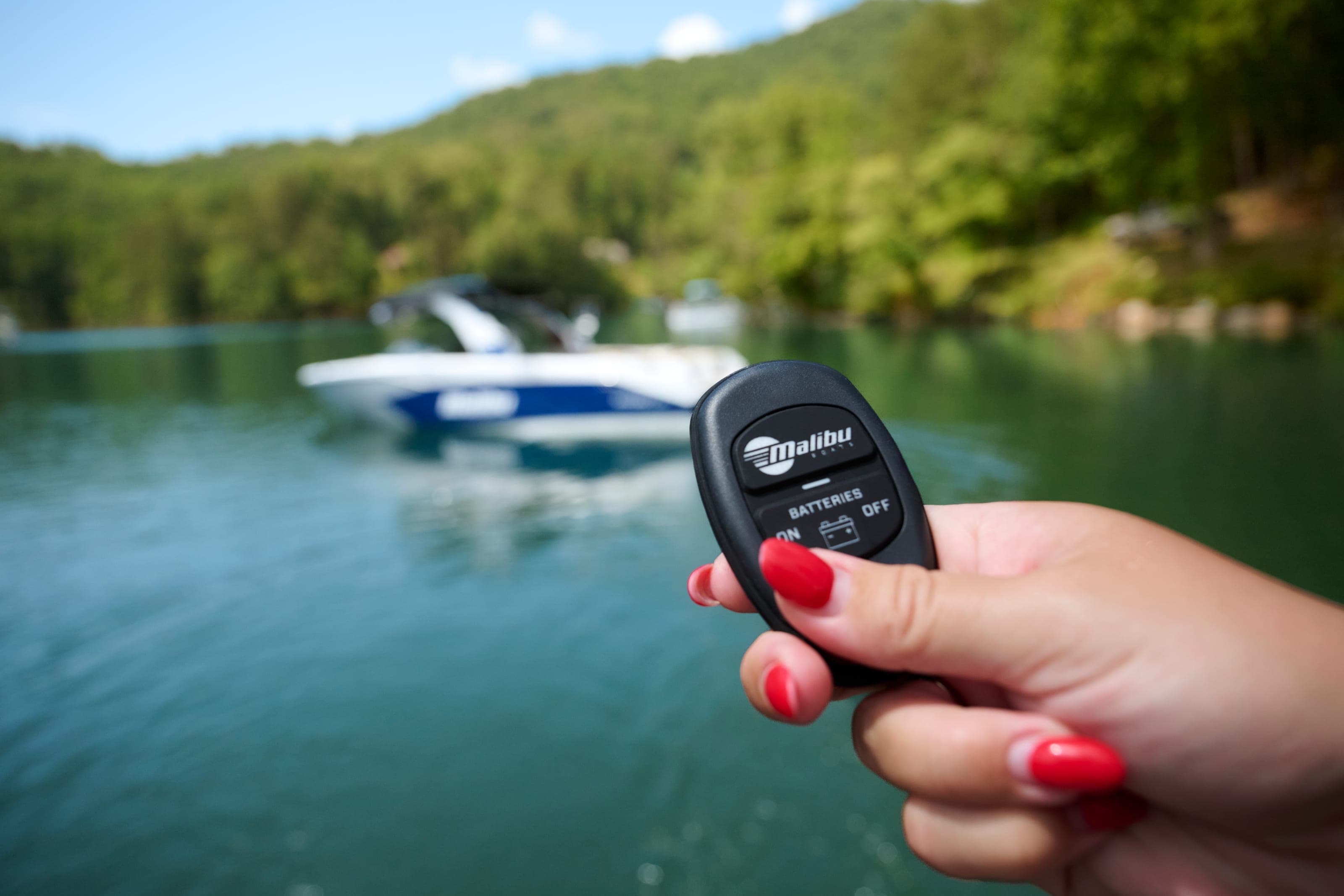 A hand holds a Malibu key fob, a Malibu boat on the water behind it